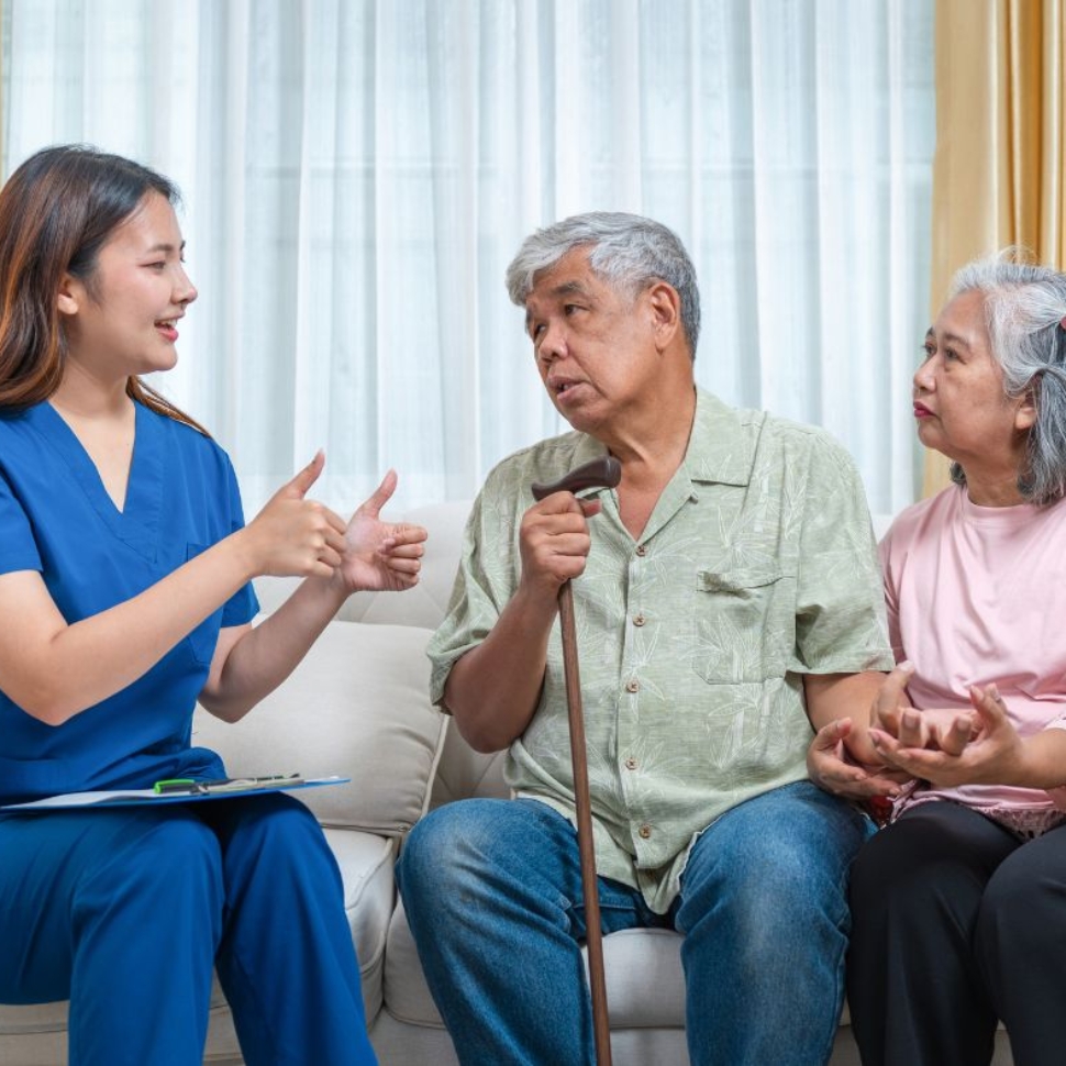 Caregiver speaking with an older couple in their home while discussing in-home care and support options